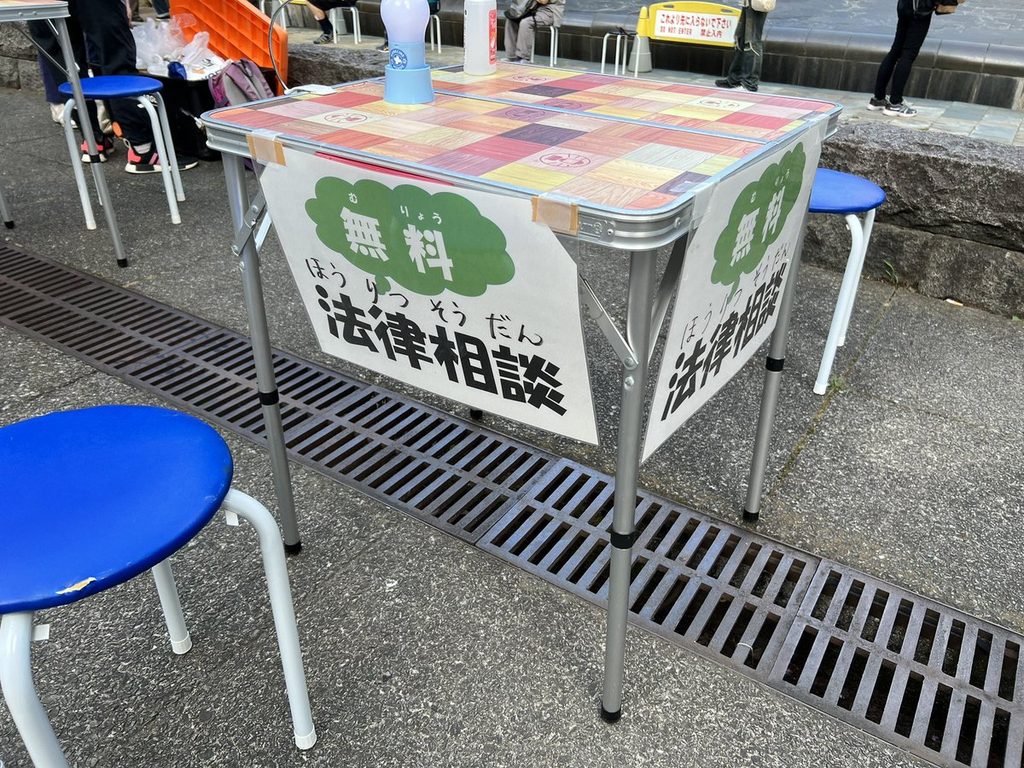 「無料 法律相談」と貼り紙のされた相談用テーブルと丸椅子