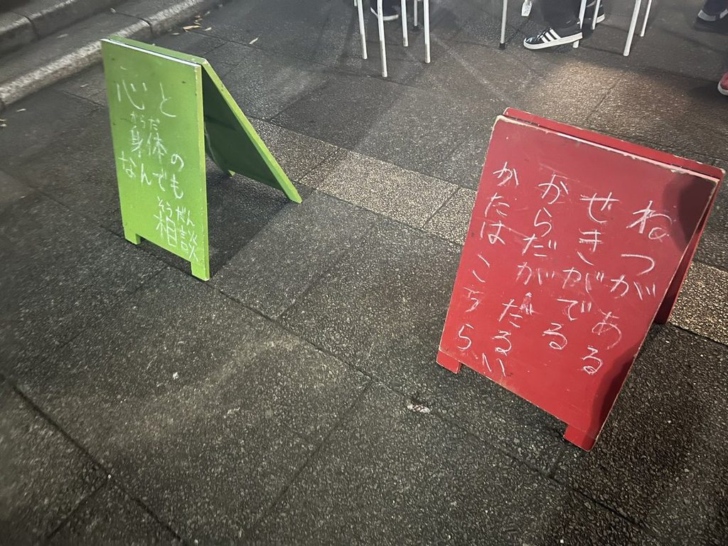 会場の路上に置かれた、緑と赤の手書きの立て看板