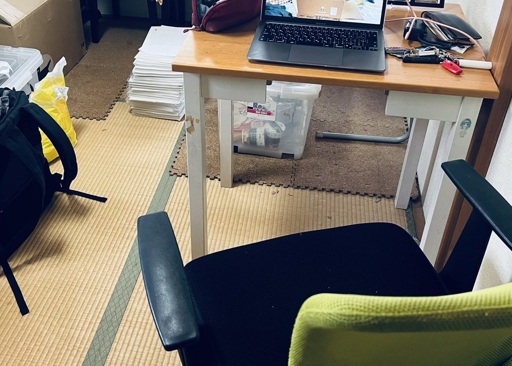 間借りした一室。机の上にノートパソコンと書類が置かれている