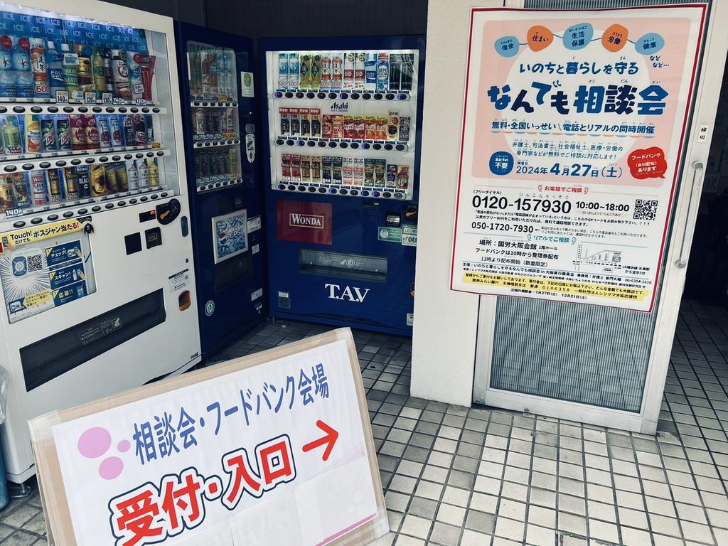 相談会の会場入口。「いのちと暮らしを守る なんでも相談会」の案内と、「相談会・フードバンク会場 受付・入口」の貼り紙