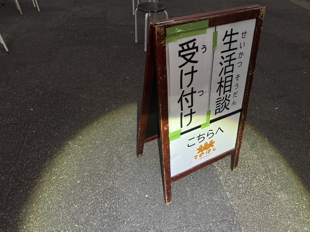 「生活相談 受け付け こちらへ」と書かれたA型看板