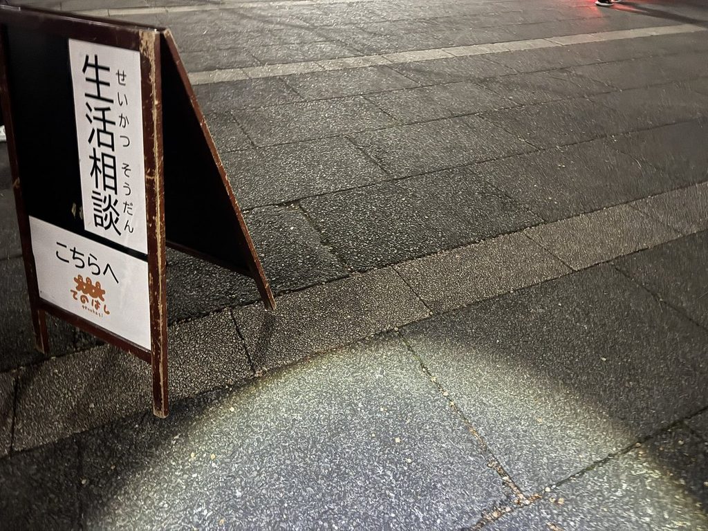 夜の会場に立つ「生活相談 こちらへ」のA型看板