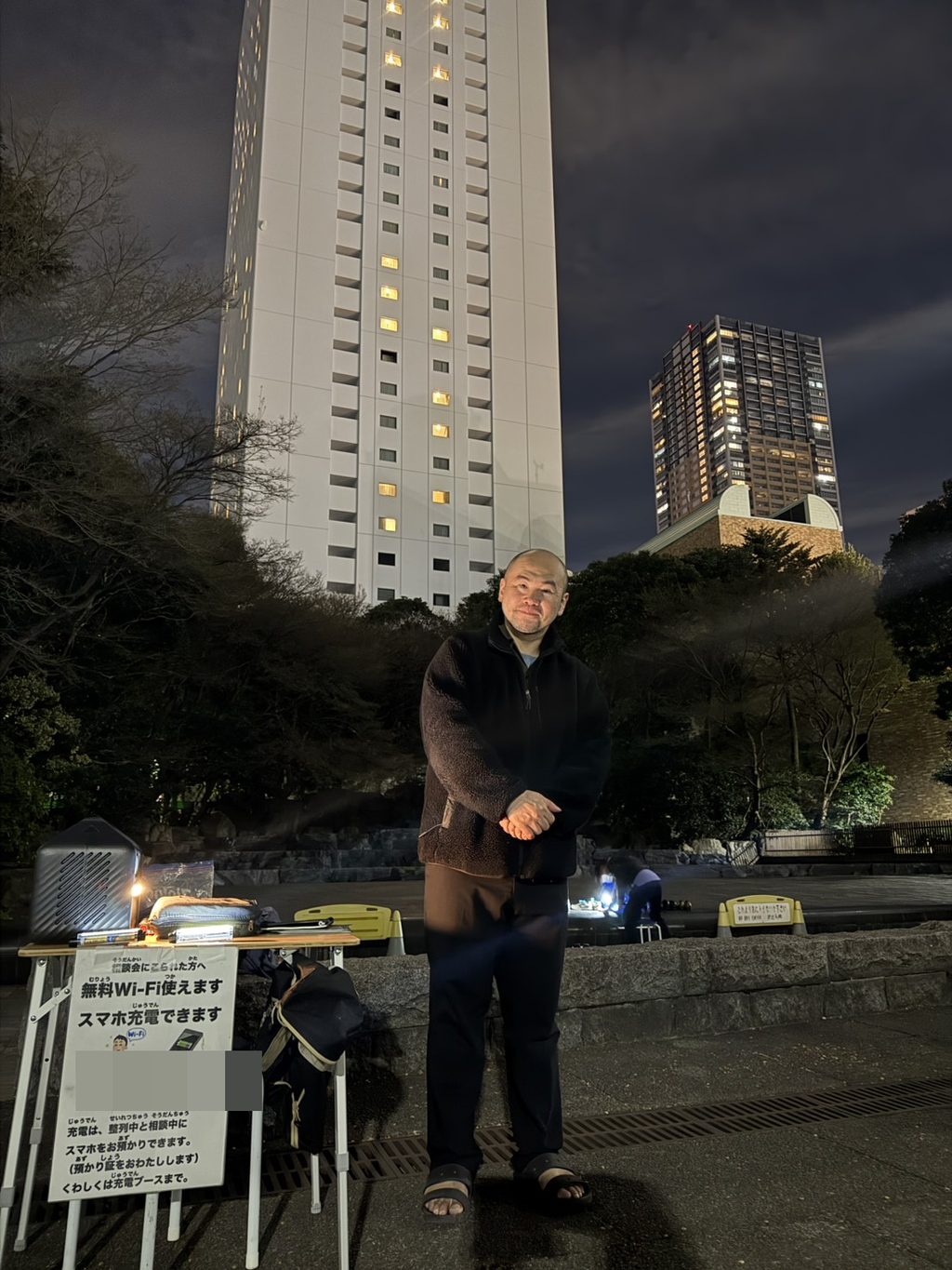 夜の東池袋中央公園に設営した相談ブース。テーブルの手前に「相談会にこられた方へ 無料Wi-Fi使えます スマホ充電できます」の貼り紙が立てられている