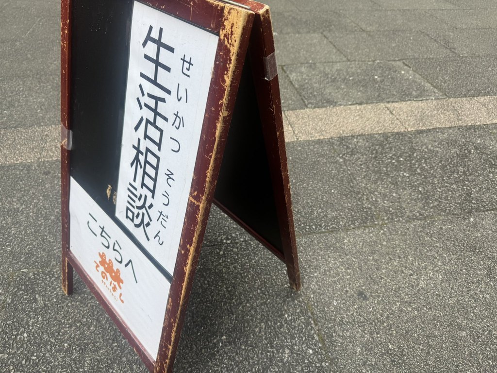 「生活相談 こちらへ」と書かれた、てのはしのA型看板。会場の路上に立てられている